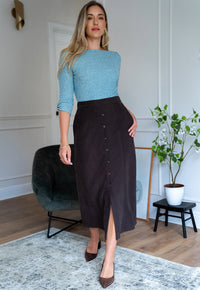 A woman models a dark brown midi skirt with a button-down front and side slit, paired with Women’s Aniz light blue boat neck knit top with three-quarter sleeves by Elizabeth Lozano